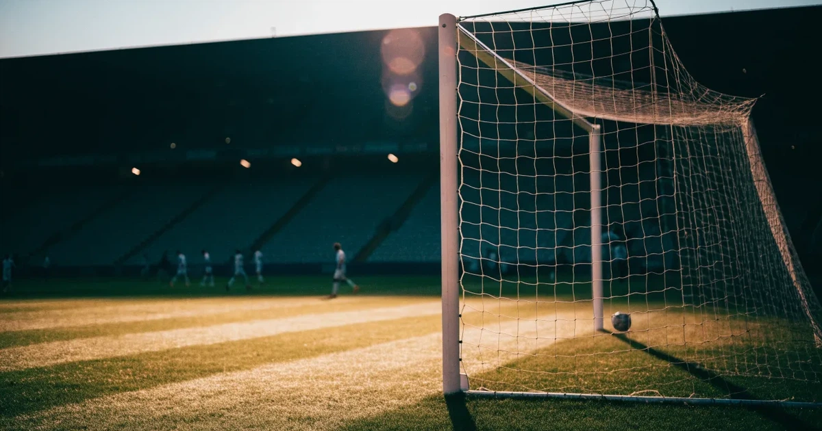 Ein Fussballtor mit weissem Netz steht auf frisch gemähtem Rasen, die hellen und dunklen Streifen im Gras leuchten im Gegenlicht.