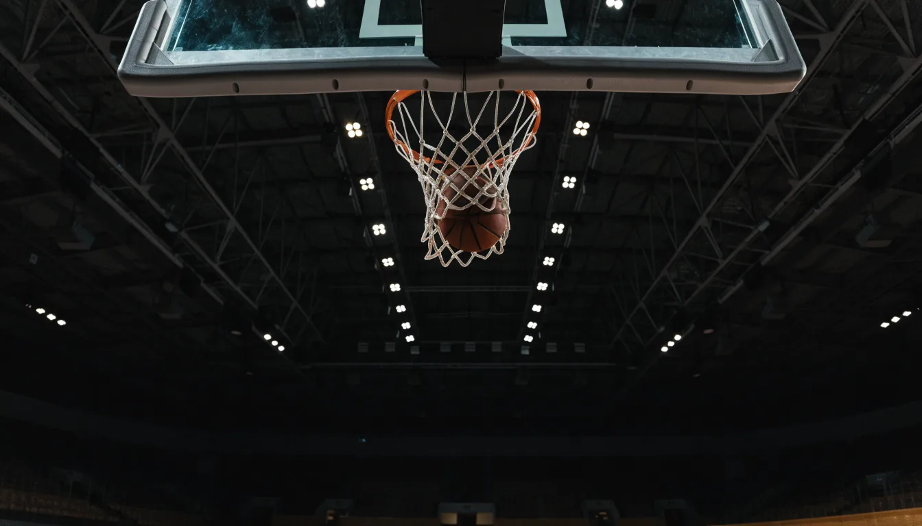 Ein Basketballkorb von unten gesehen, darüber eine Hallendecke mit Scheinwerfern und Stahlträgern.