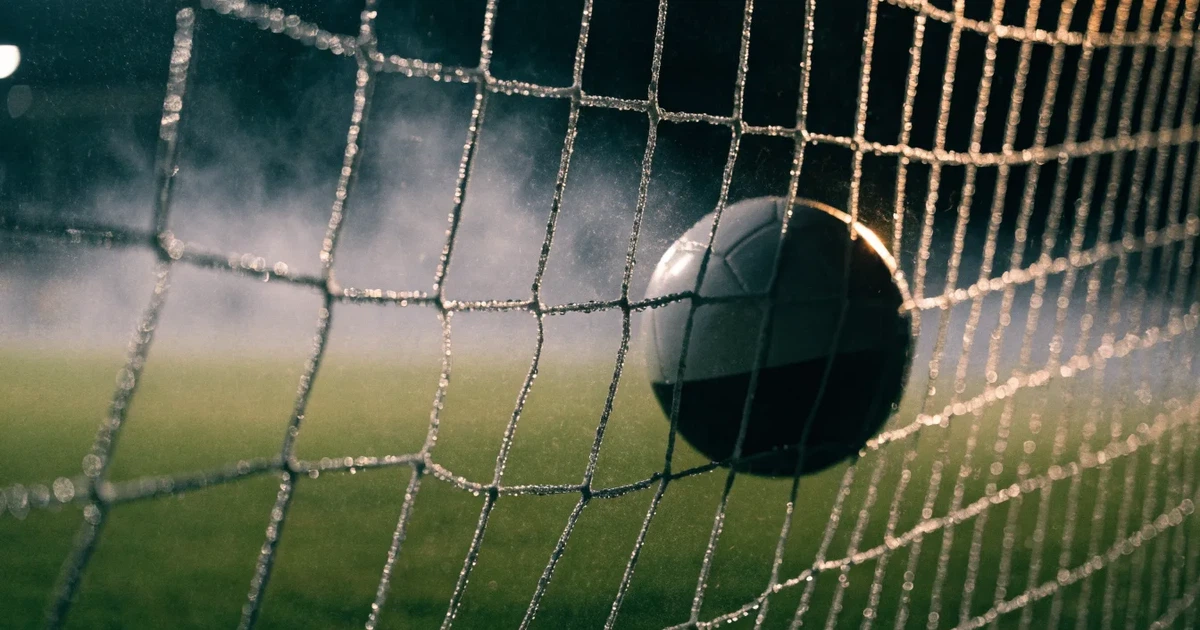 Ein Fussballnetz in Nahaufnahme, in dem ein Ball hängt, Wassertropfen glänzen auf den Maschen.