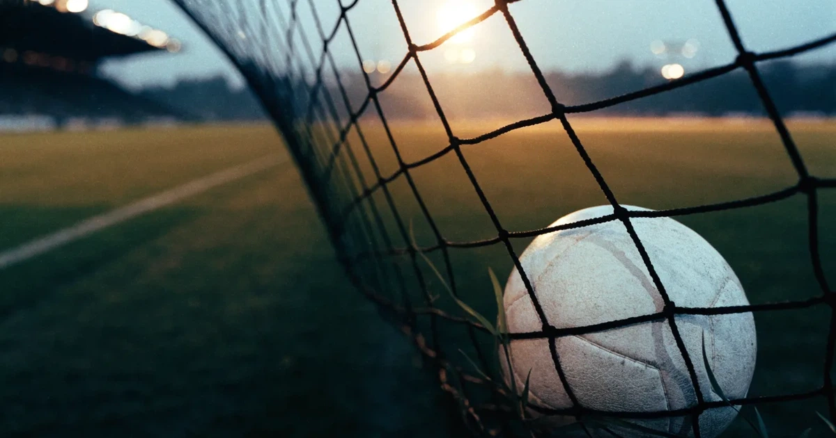 Ein Fussball liegt im Netz eines Tores, Flutlicht und kalte Abendluft liegen über dem leeren Platz