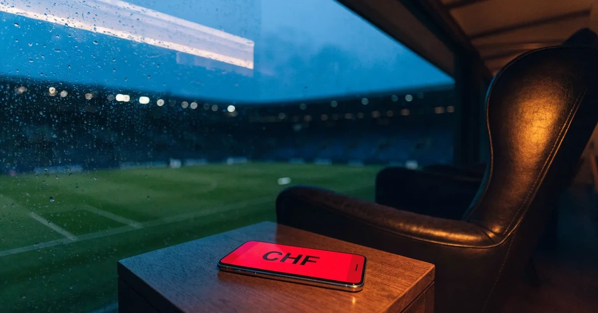 Ein leerer Ledersessel steht in einer Stadionloge mit Blick auf das Spielfeld im Abendlicht.