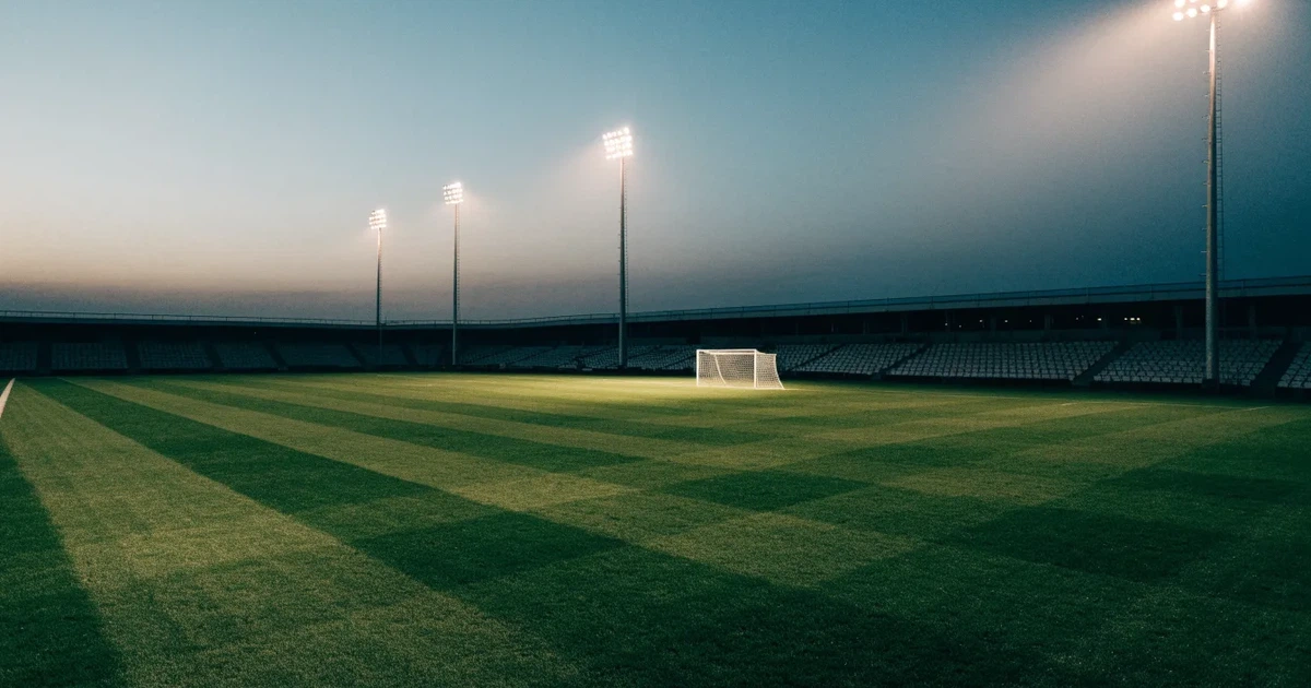 Ein menschenleerer Fussballplatz mit frisch gemähtem Rasen unter Flutlichtmasten in der Abenddämmerung, aus erhöhter Perspektive fotografiert.