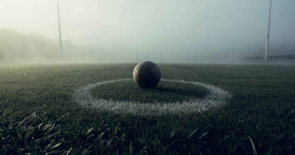 Ein Fussball liegt auf dem Anstosspunkt eines leeren Rasenplatzes im dichten Morgennebel.